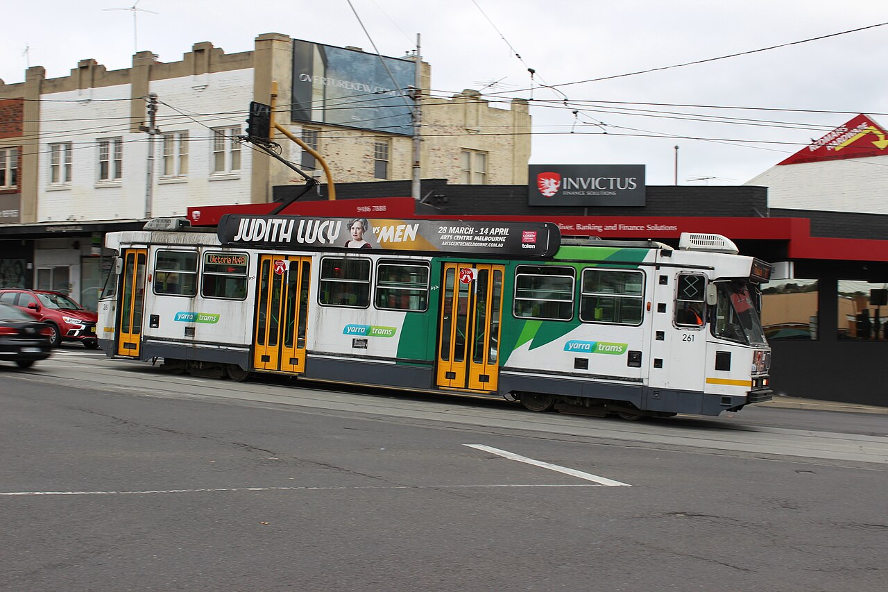 A-class tram passing shops at a suburban intersection