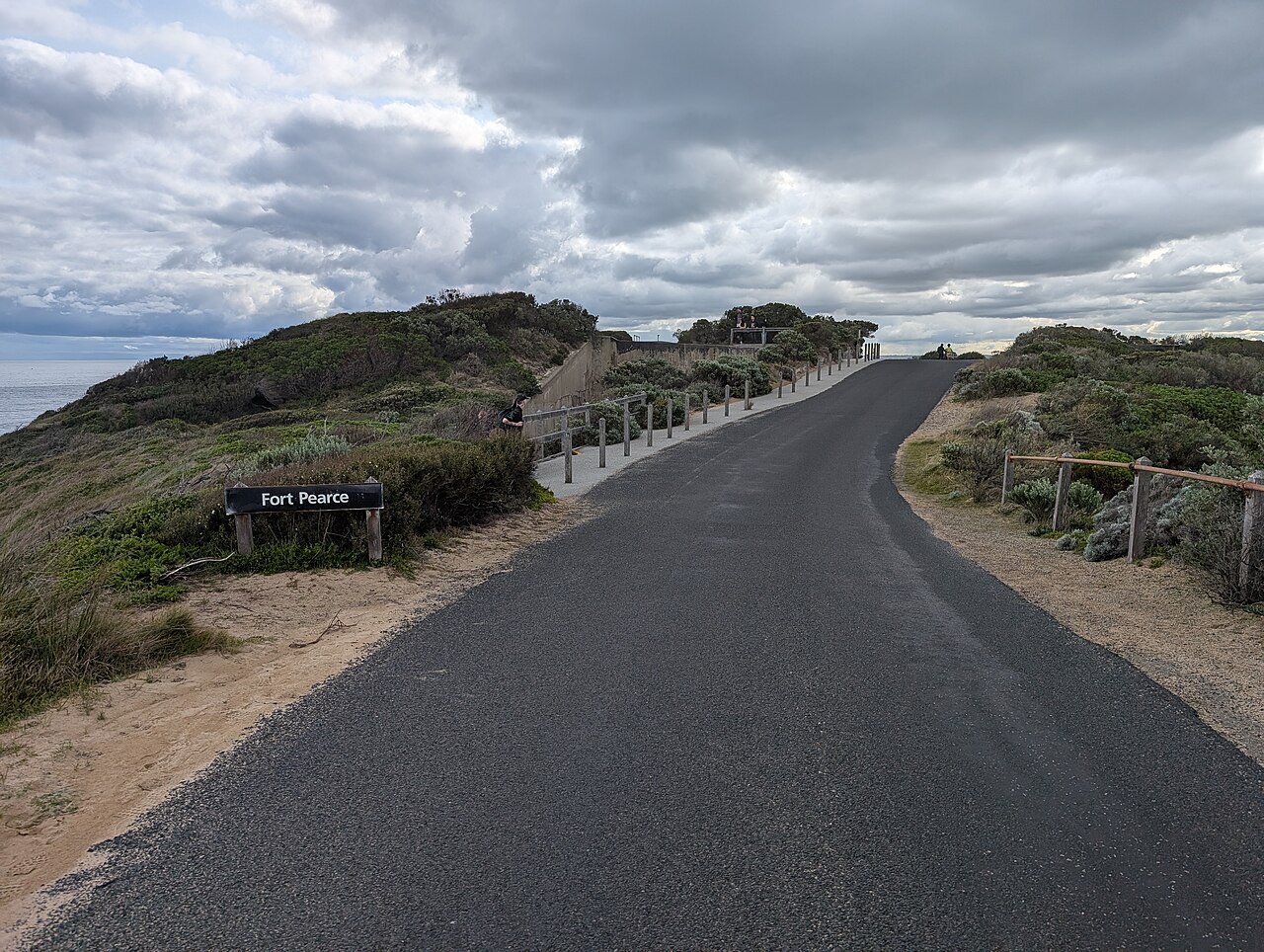 Defence Road winding through coastal scrub, with an entrance sign